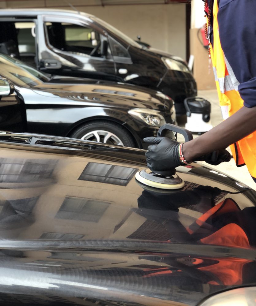 Detailer machine-polishing a black bonnet to a mirror finish